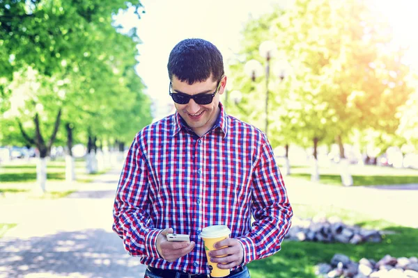 The man in the summer in the park, reading a message on your phone, glasses, watching the map and news feed  social networks, happy smiles   video film in jeans bright sunny day. Idea concept