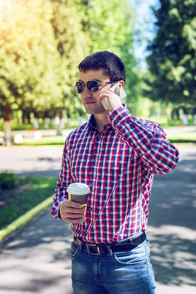 Man in  shirt and jeans  glasses, talking on the phone,  smartphone, the concept of summer,  businessman  vacation. City lifestyle.  the street in the park.