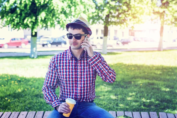 Man in  shirt and jeans  glasses, talking on the phone,  smartphone, the concept of summer,  businessman  vacation. City lifestyle.  the street in the park.