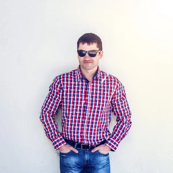 The man in the summer against the wall, glasses, serious looks in front, in jeans and a shirt,  bright sunny day. The idea of the concept   businessman in the city, for an inscription on  white