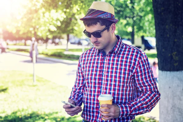 Man in  shirt and jeans  sunglasses, holding  mobile phone coffee or tea, read the conversation messages on your , the concept of summer,  businessman  vacation. City lifestyle.  the street in the