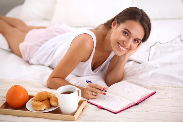 Young beautiful woman lying in bed writing a diary