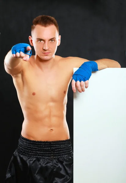 Young handsome boxer man standing near board and pointing at you, isolated on black background