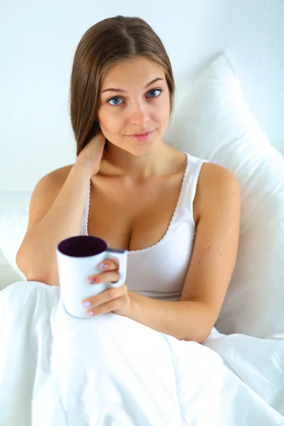 A pretty young woman in bed enjoying a cup of tea