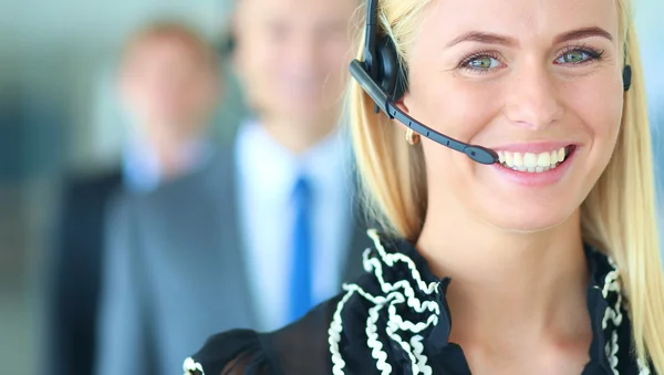 Businesswoman with headset smiling at camera in call center. Businessmen in headsets on background