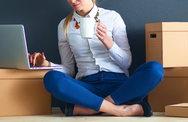 Woman sitting on the floor near a boxes  with laptop