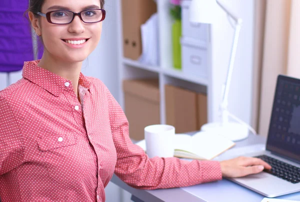 Young attractive female fashion designer working at office desk, drawing while talking on mobile