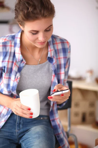 Smiling woman holding her cellphone in the kitchen