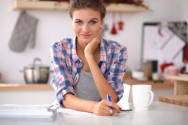 Smiling woman with cup of coffee and newspaper in the kitchen