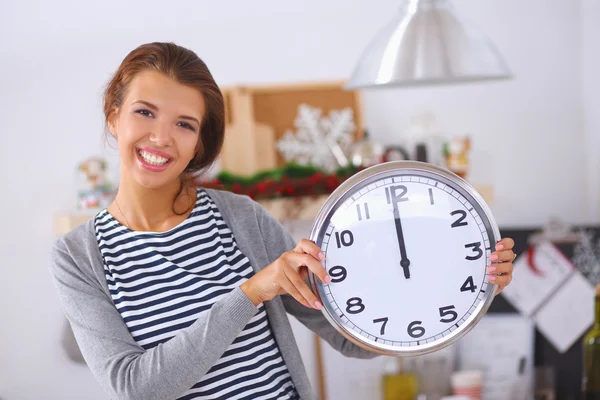 Happy young woman showing clock in christmas decorated kitchen