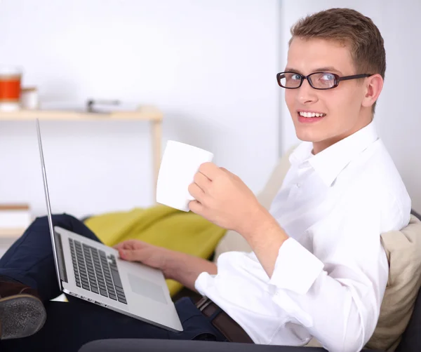 Relaxed attractive man holding coffee while working on his laptop in bright living room