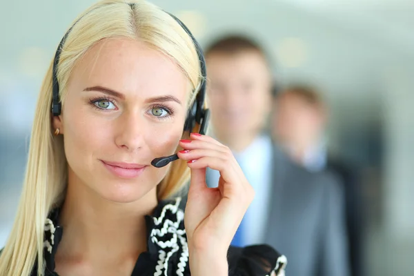 Businesswoman with headset smiling at camera in call center. Businessmen in headsets on background