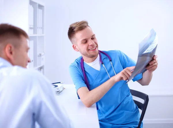 Portrait of a smiling male doctor with laptop sitting at desk in medical office