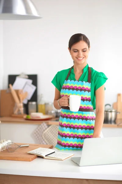Smiling young woman standing in the kitchen with cup