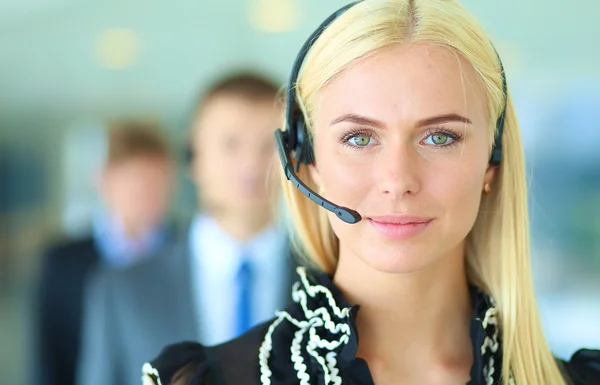 Businesswoman with headset smiling at camera in call center. Businessmen in headsets on background