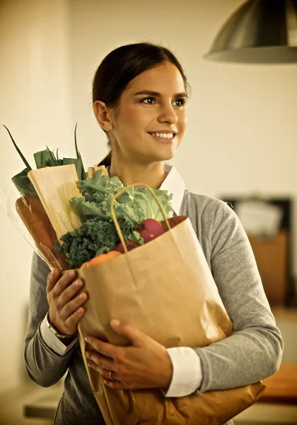 Young woman holding grocery shopping bag with vegetables Standing in the kitchen.