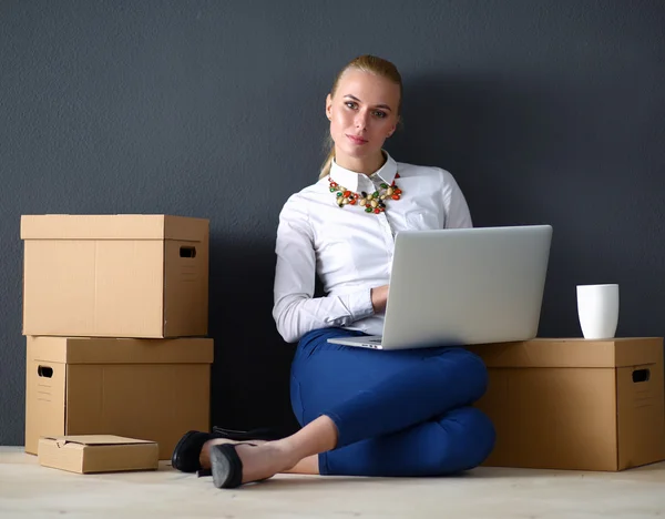 A young businesswoman sitting on the floor working on a laptop while surrounded by boxes