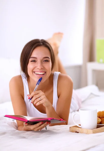 Young beautiful woman lying in bed writing a diary