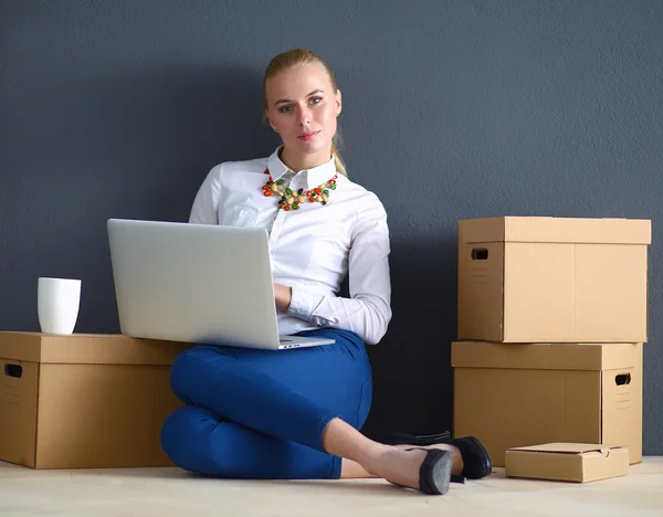 A young businesswoman sitting on the floor working on a laptop while surrounded by boxes