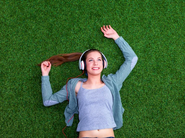 Relaxed woman listening to the music with headphones lying on  grass
