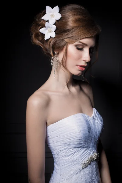 Beautiful sweet gentle girl groom in a wedding dress with a wreath and flowers in her hair in the studio