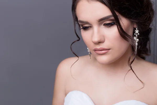 Beautiful gentle girl portraits of the bride in a white wedding dress with evening hairstyle with a rim of flowers in her hair and make-up in studio