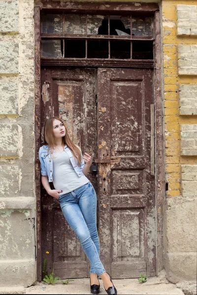 Beautiful young sweet girl with red hair in jeans standing near the door of the old city