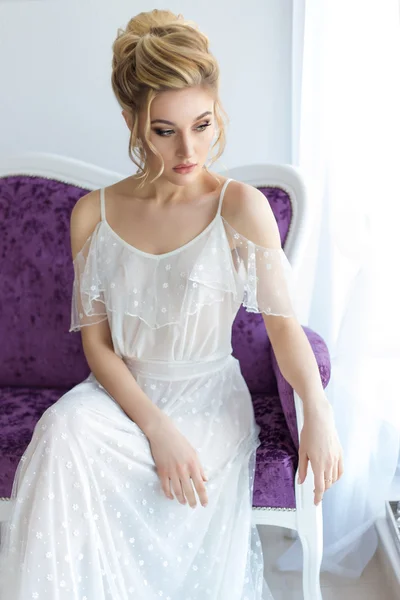 Beautiful cute sweet young girl in a light dress beautiful boudoir with bright makeup smokey eyes with a beautiful evening hairstyle and jewelry handmade