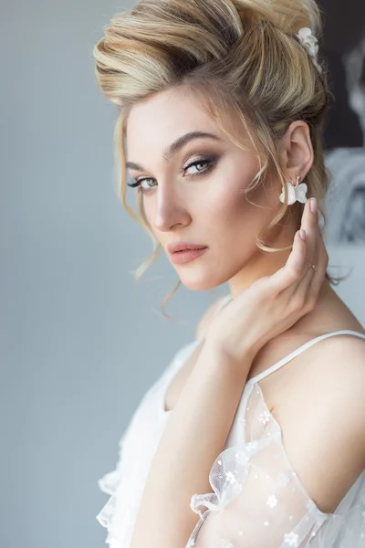 Beautiful cute sweet young girl in a light dress beautiful boudoir with bright makeup smokey eyes with a beautiful evening hairstyle and jewelry handmade