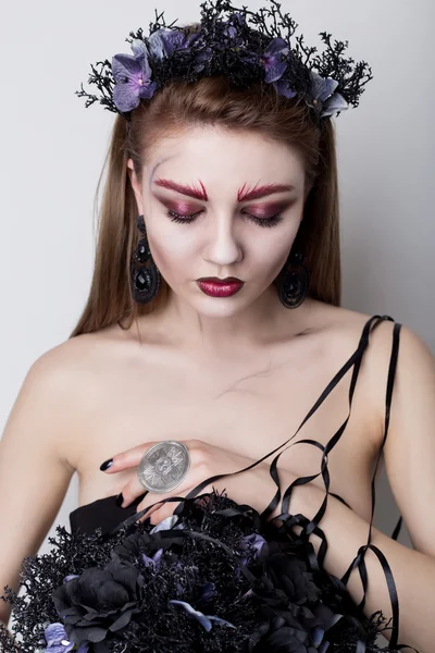 Beautiful cheeky girl in the image of a vampire with bright dark makeup, black vampire bride with a bouquet and a black wreath