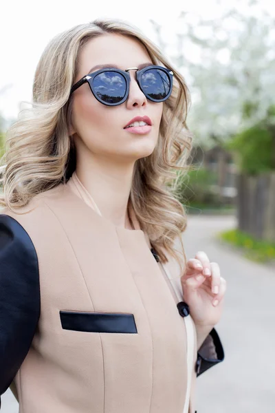 Portrait of a beautiful cute sexy funny girl in sunglasses with a beautiful smile in a coat walks on city streets