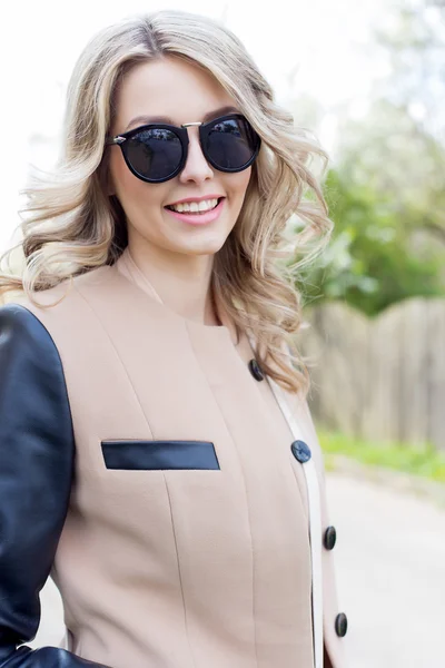 Portrait of a beautiful cute sexy funny girl in sunglasses with a beautiful smile in a coat walks on city streets
