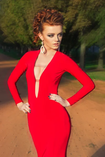 Beautiful elegant girl with beautiful makeup and hair in a red evening dress in the Park
