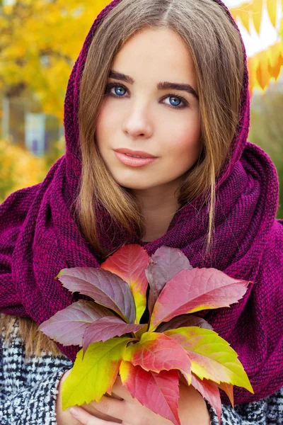 Beautiful charming young attractive girl with large blue eyes with a handkerchief on his head, long dark hair holding a fall bouquet of leaves on a cold autumn day