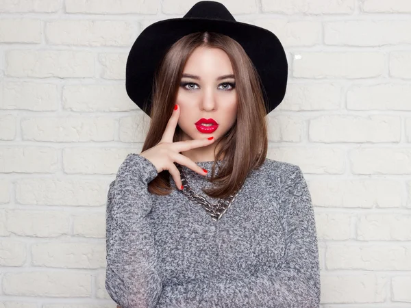 Beautiful sexy young girl in a black hat with red full lips, bright makeup and painted my nails red