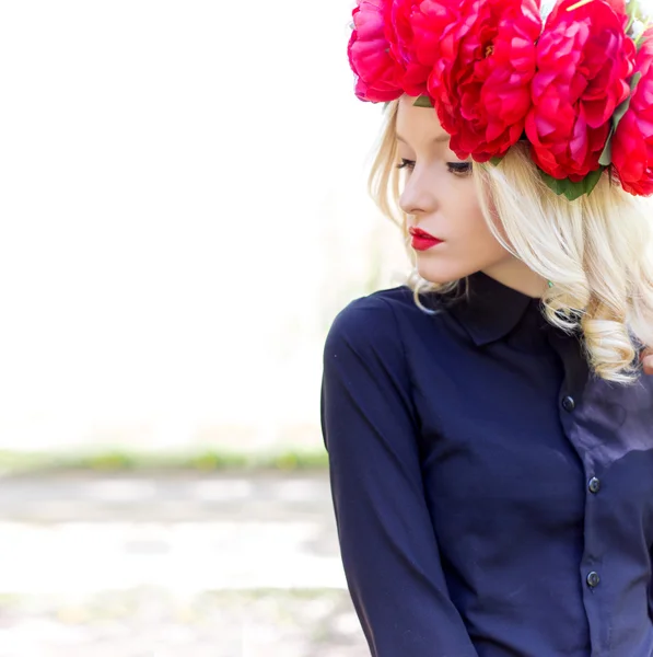 Beautiful young gentle elegant young blond woman with a red crown of peony in a black blouse walks in the lush apple orchard