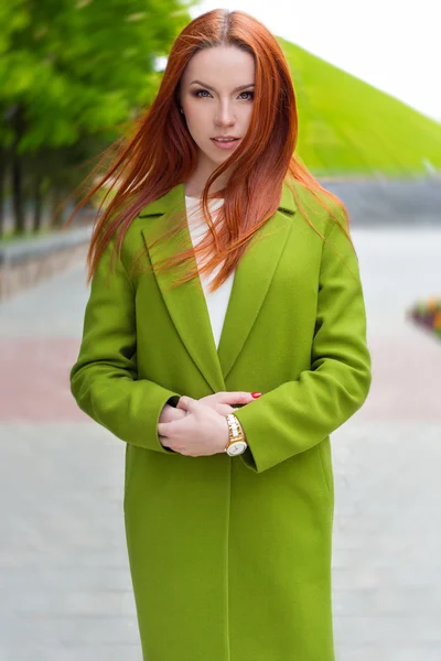 Beautiful sexy woman with fiery red hair with green coat walking through the streets of the city