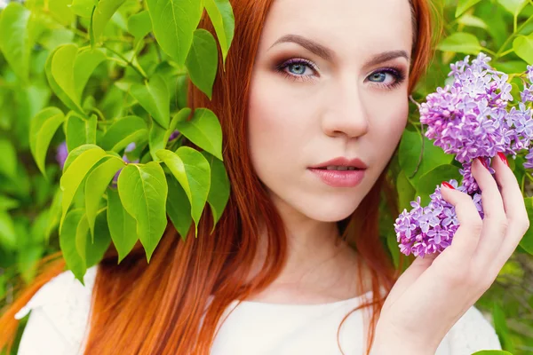 Beautiful cute sexy red-haired girl with long hair in a white dress with a bouquet of lilac in the hands of