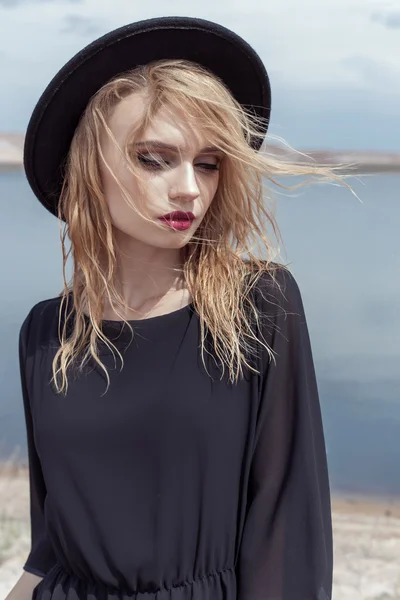 Fashion photo of young beautiful sexy girl with wet hair in a black hat and a black cotton dress with beautiful bright makeup, model proportionally