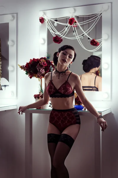 Beautiful sexy young woman flaunts front of the mirror in the dressing room in lacy underwear in a retro style with bright make-up and beautiful evening hairstyles , shot in the style of the 20s