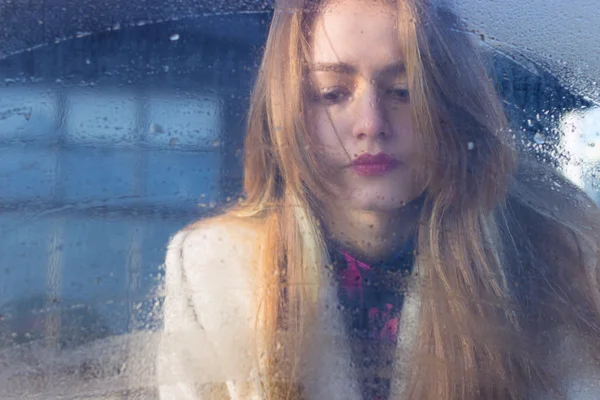 Sad beautiful seksalnaya Pretty sad lonely girl behind wet glass with big sad eyes in a coat