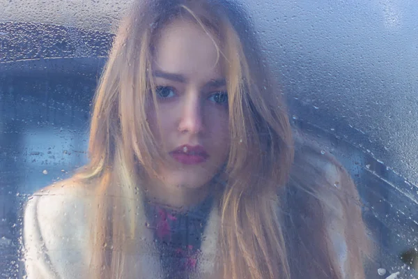 Sad beautiful seksalnaya Pretty sad lonely girl behind wet glass with big sad eyes in a coat