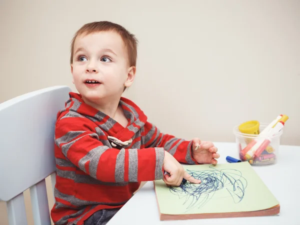 Portrait of cute Caucasian white little boy toddler drawing with color pencils markers on paper in album, looking surprised, excited, looking away