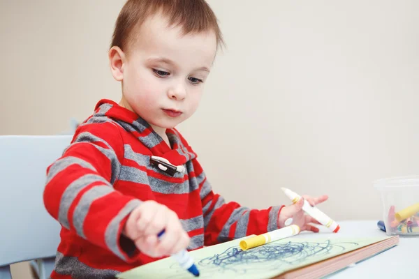 Portrait of cute Caucasian white little boy toddler drawing with color pencils markers on paper in album, looking serious, engaged in process