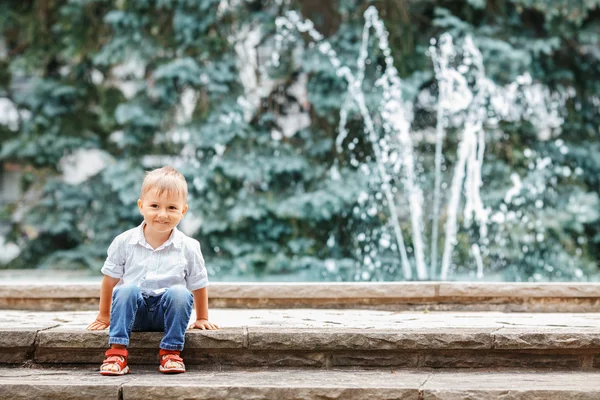 Portrait of cute adorable funny Caucasian  little boy toddler in white shirt and blue jeans playing laughing smiling having fun by fountain in summer outside