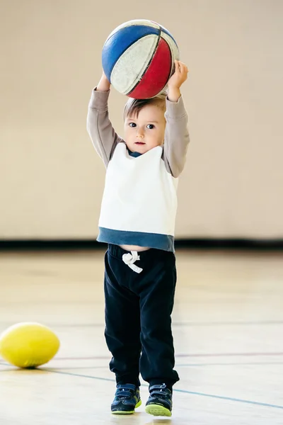 Cute adorable little small white Caucasian child toddler boy playing with ball basketball in gym on plain white light background, having fun, healthy lifestyle childhood concept