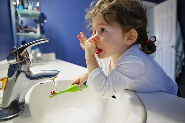 Closeup portrait of  child toddler girl in bathroom toilet washing face hands brushing teeth with toothbrash playing with water, lifestyle home style, everyday moment, morning routine