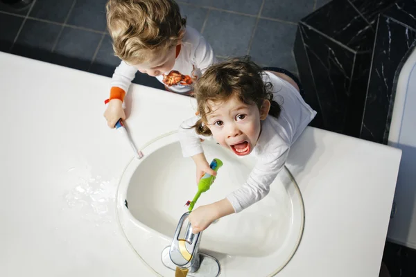 Closeup portrait of twins kids toddler boy girl in bathroom toilet washing face hands brushing teeth with toothbrash playing with water, lifestyle home style, everyday moments, top view