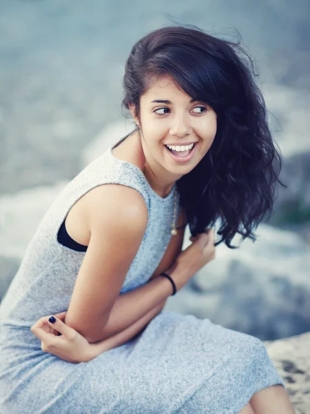 Portrait of beautiful Hispanic latino white girl woman with brown eyes, long dark curly wavy hair in gray dress sitting in park outside smiling laughing looking away, lifestyle portrait concept