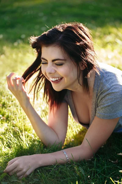 Closeup portrait of beautiful smiling young Caucasian woman with red black hair, lying on grass outdoors, laughing showing teeth, natural beauty youth look